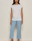 Woman wearing a white sleeveless top and light blue jeans against a plain background