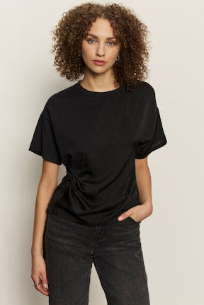 Person wearing a black t-shirt with a knot detail against a plain background