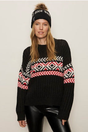 Person wearing a black sweater with colorful patterns and a matching beanie on a plain background