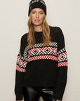 Person wearing a black sweater with colorful patterns and a matching beanie on a plain background