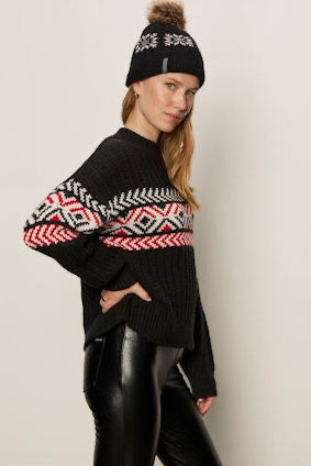 Woman wearing a black sweater with geometric patterns and a matching beanie on a plain background