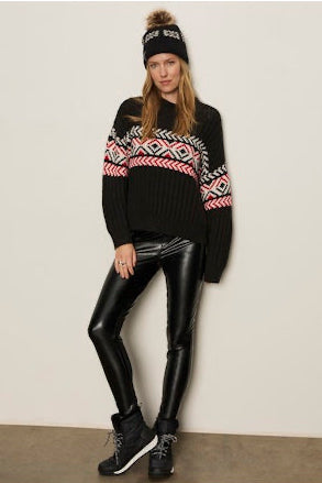 Person wearing a patterned sweater, black leggings, and a beanie against a plain background