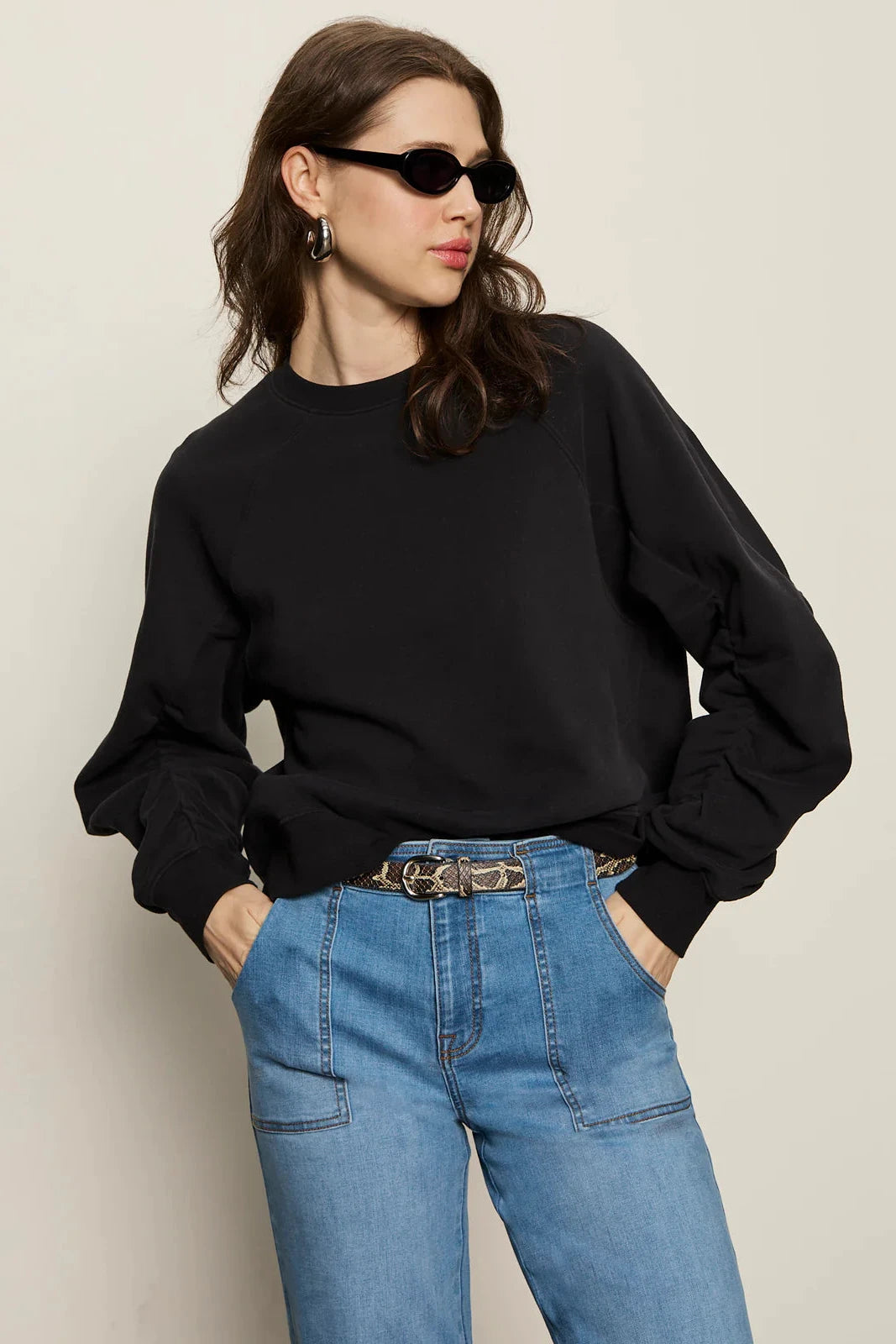 Woman wearing a black sweater and blue jeans against a plain background