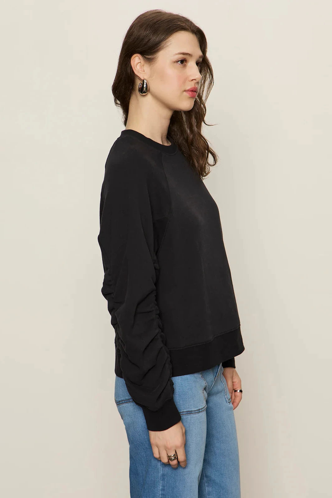 Woman wearing a black sweater and blue jeans against a plain background