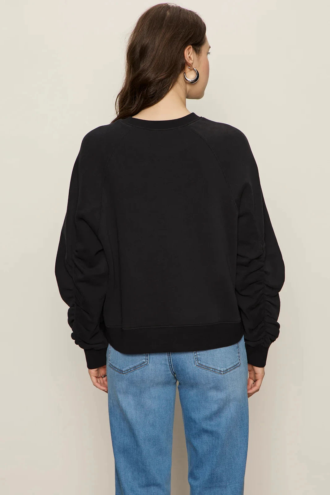 Person wearing a black sweatshirt and blue jeans on a plain background