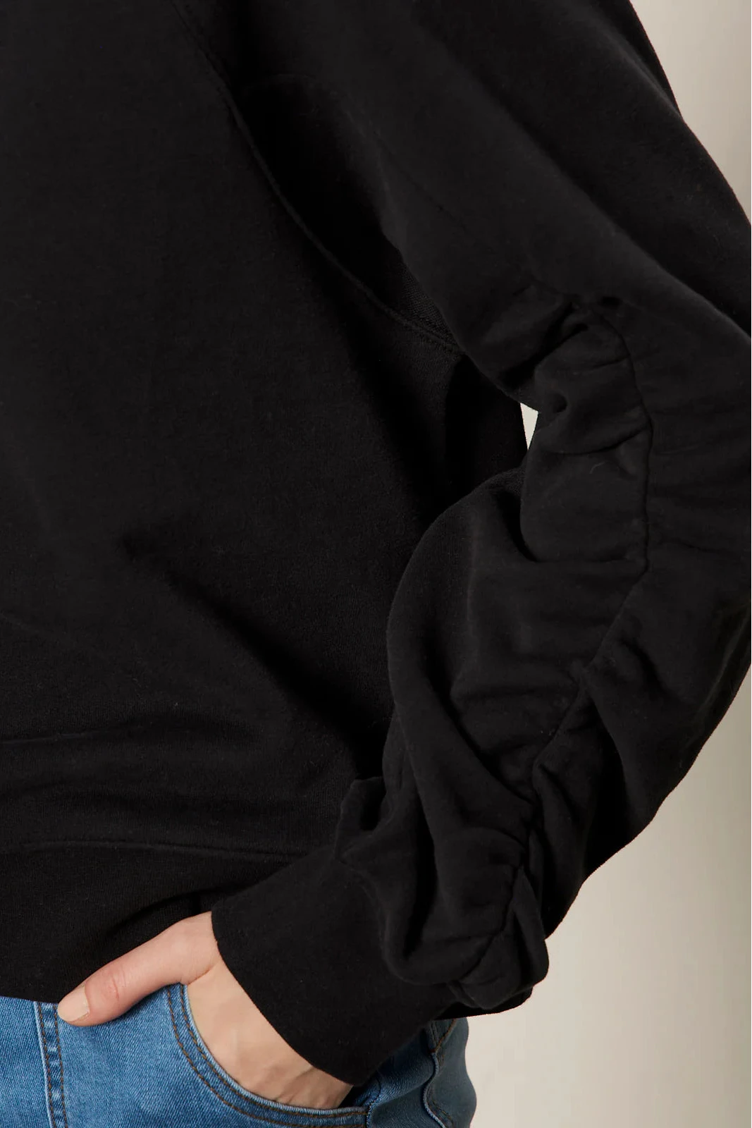 Close-up of a person wearing a black long-sleeve shirt with blue jeans.