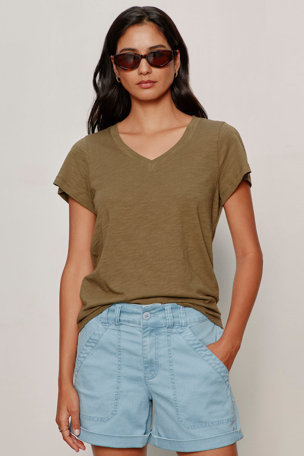 Woman wearing an olive green t-shirt and light blue shorts against a plain background