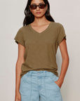 Woman wearing an olive green t-shirt and light blue shorts against a plain background
