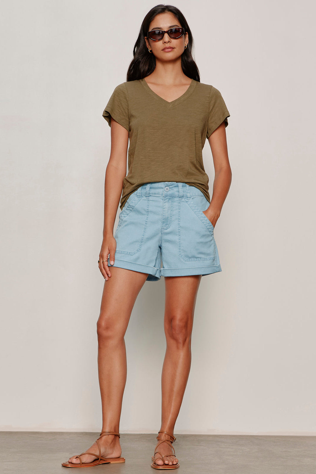 Woman wearing an olive green t-shirt and light blue shorts against a plain background