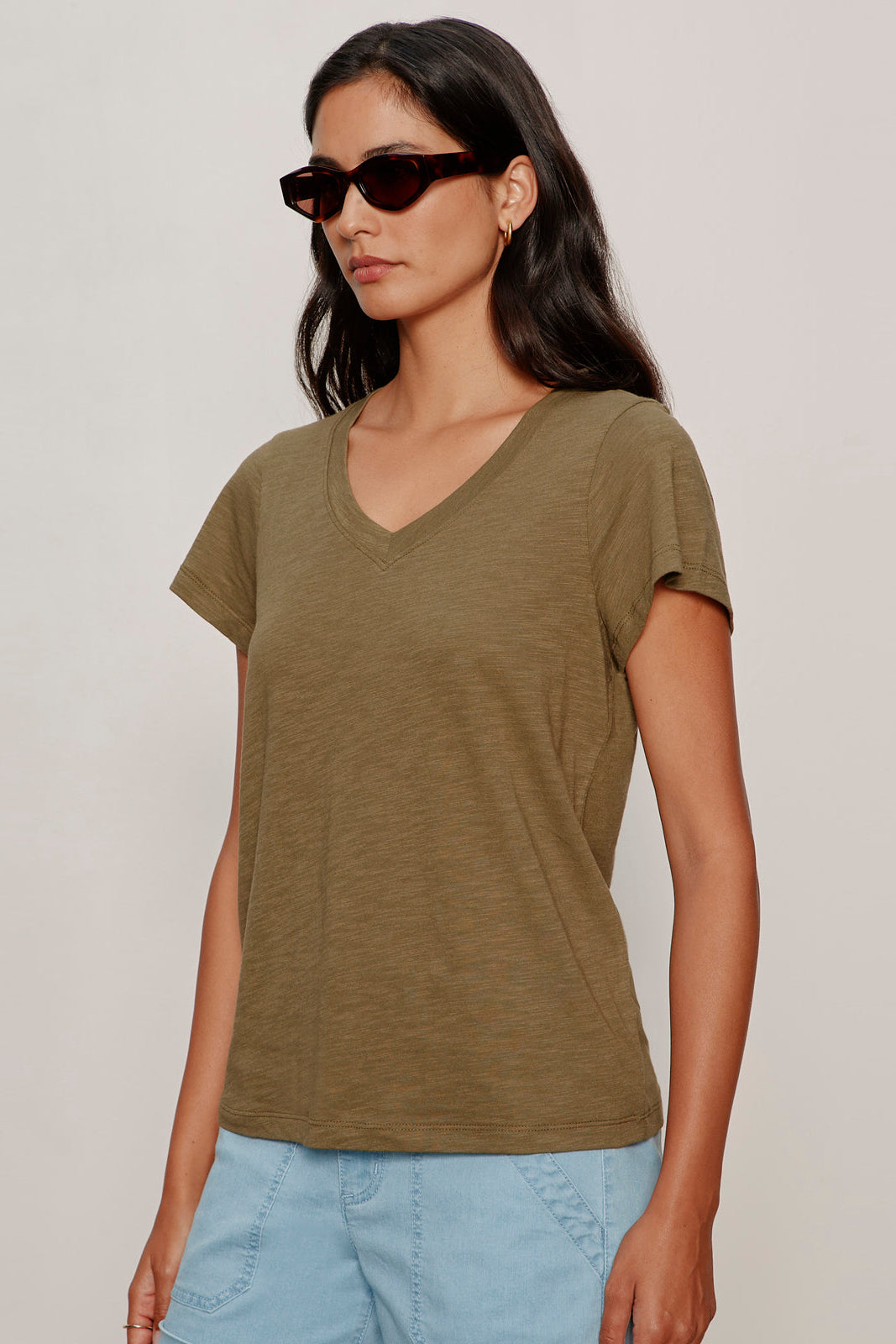 Woman wearing a green t-shirt and sunglasses against a plain background