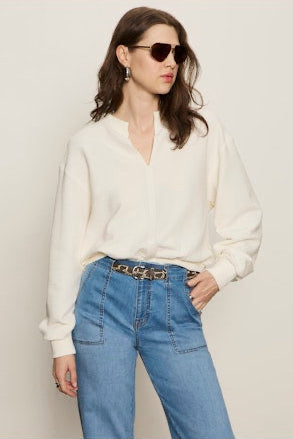 Woman wearing a white blouse and blue jeans with sunglasses against a plain background