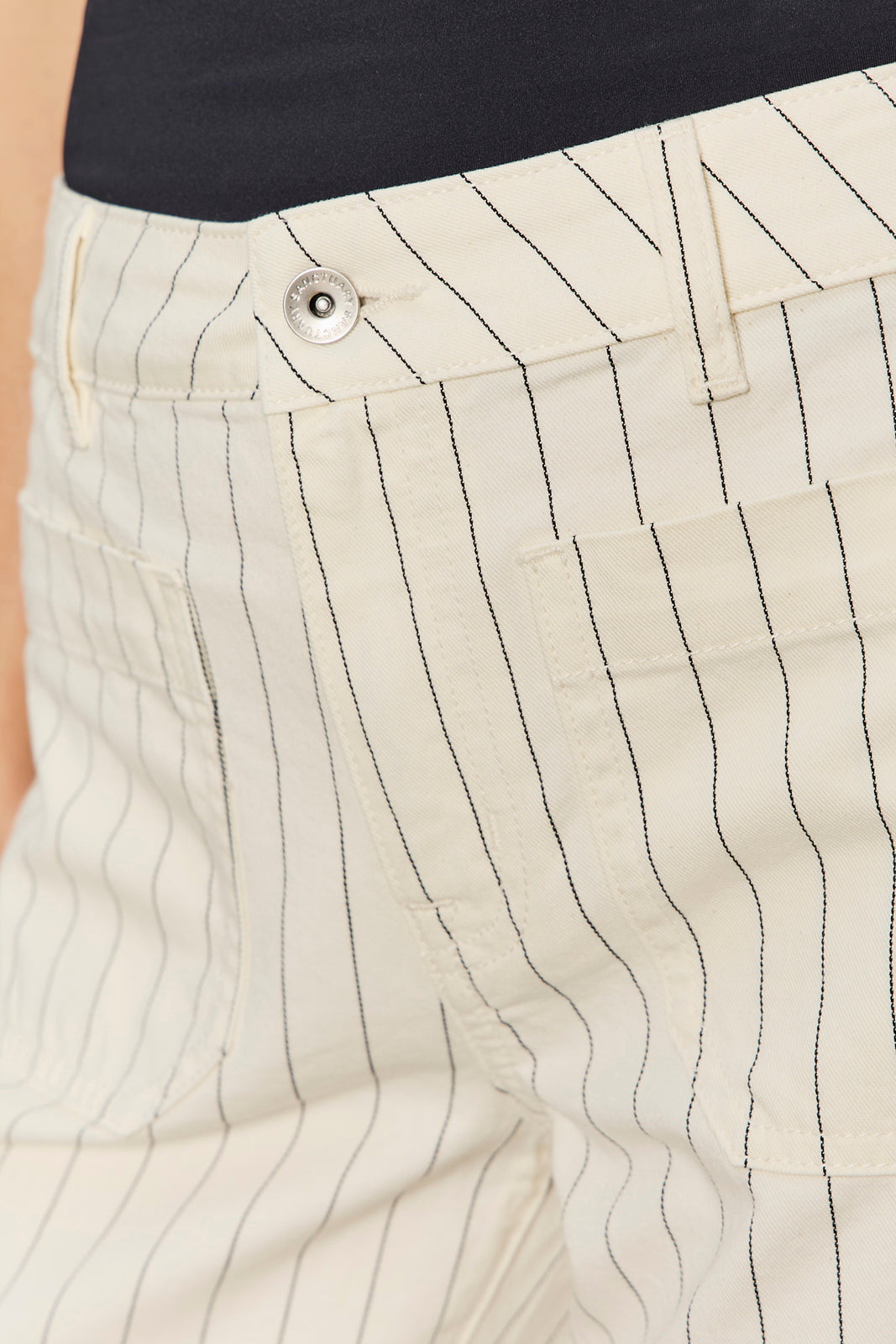Close-up of beige pants with black vertical stripes and a button.