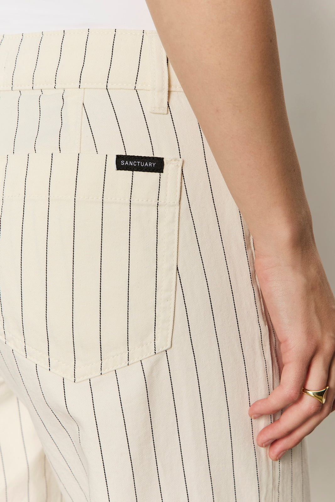 Close-up of a person wearing beige pinstripe pants with a visible brand label, on a neutral background.