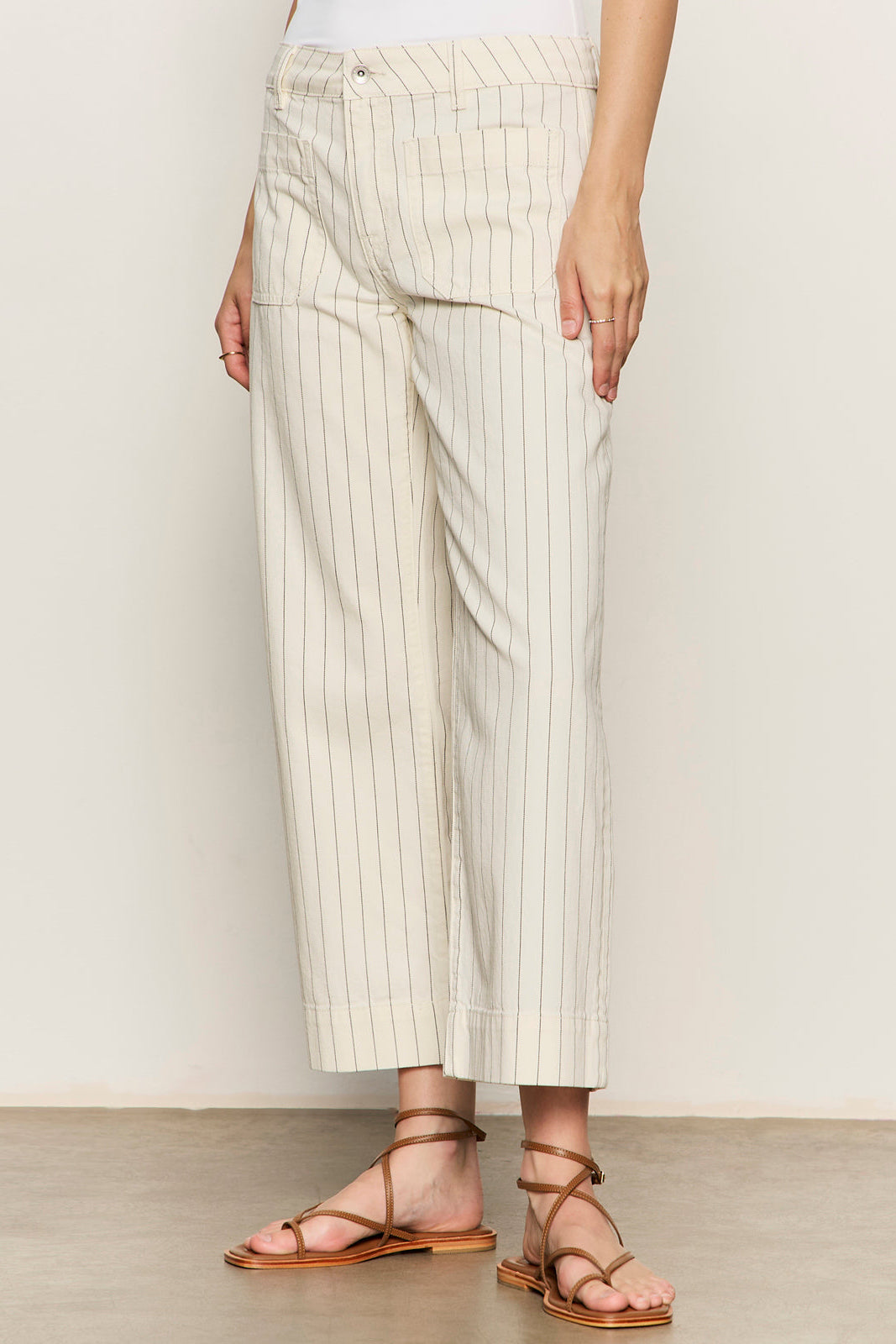Person wearing white pants with thin black stripes and strappy sandals on a plain background