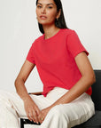 Woman wearing a red shirt and white pants sitting on a black chair against a white background