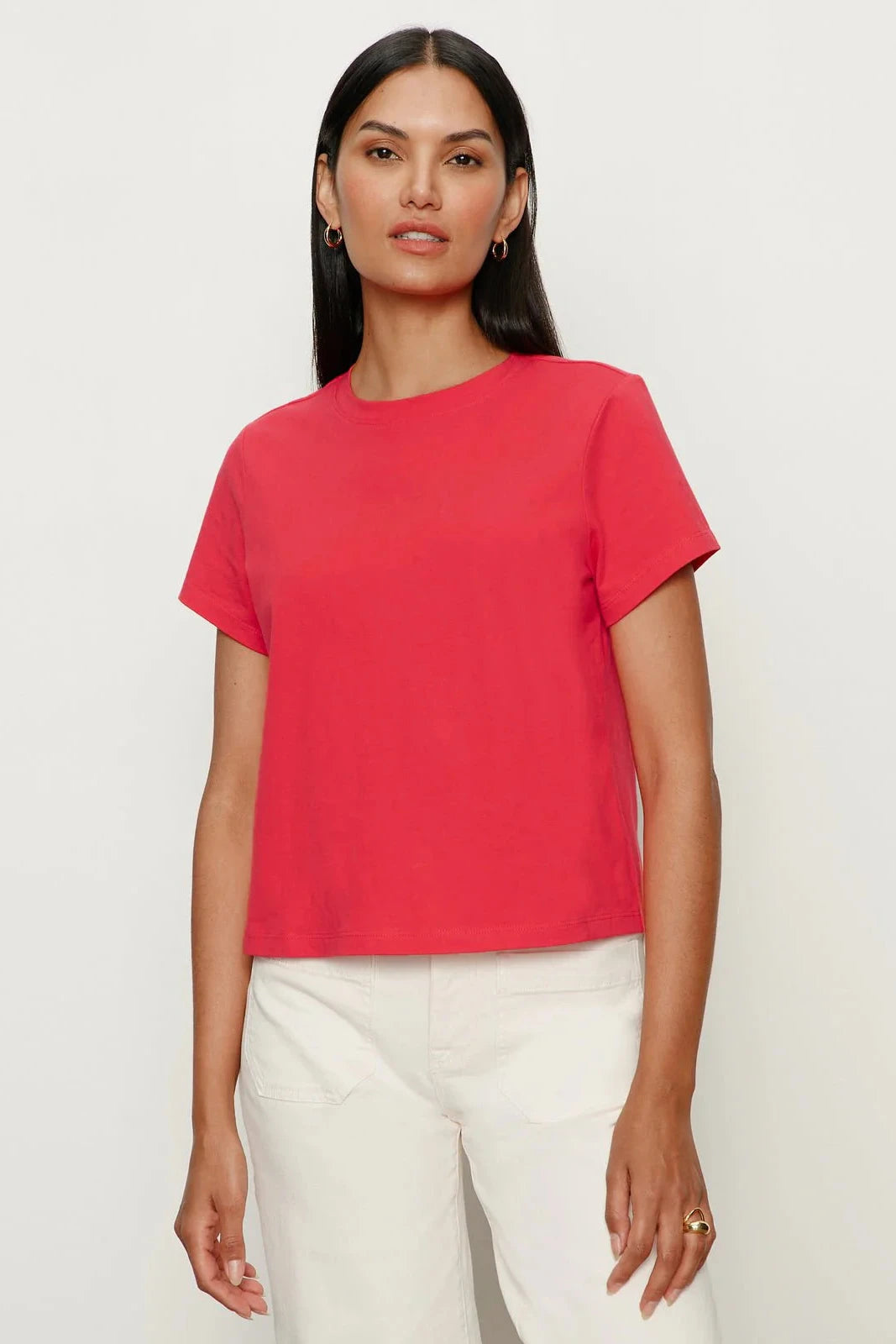 Woman wearing a red t-shirt and white pants on a plain background