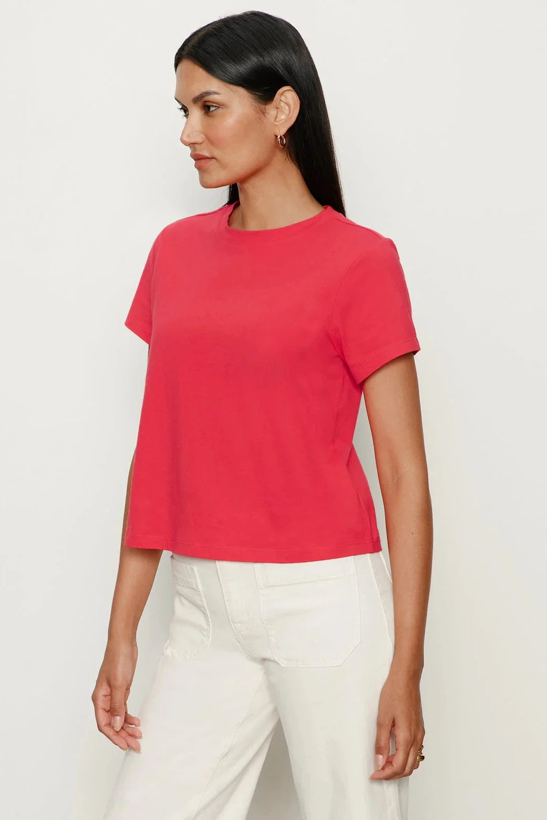 Woman wearing a red t-shirt and white pants on a light gray background