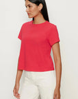 Woman wearing a red t-shirt and white pants on a light gray background