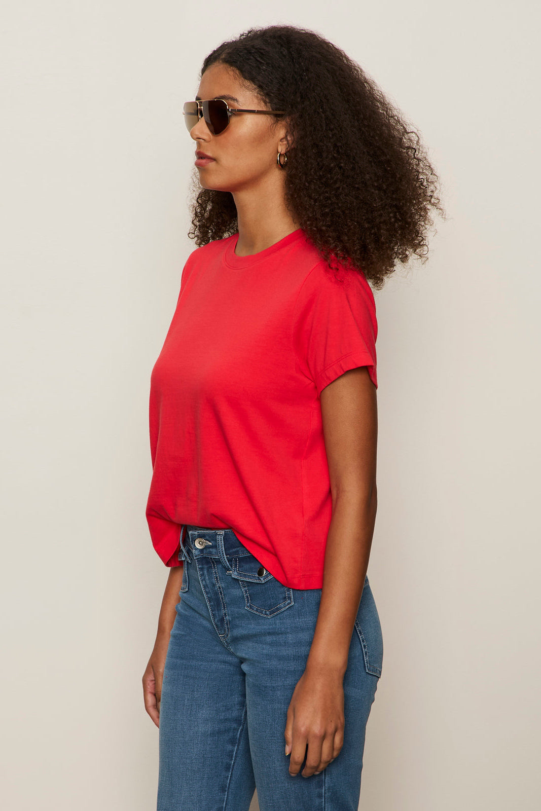 Woman wearing a red shirt and blue jeans against a plain background