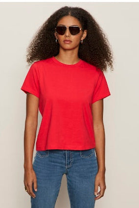 Woman wearing a red t-shirt and blue jeans against a plain background