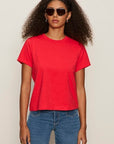 Woman wearing a red t-shirt and blue jeans against a plain background