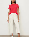 Woman wearing a red t-shirt and white pants against a plain background