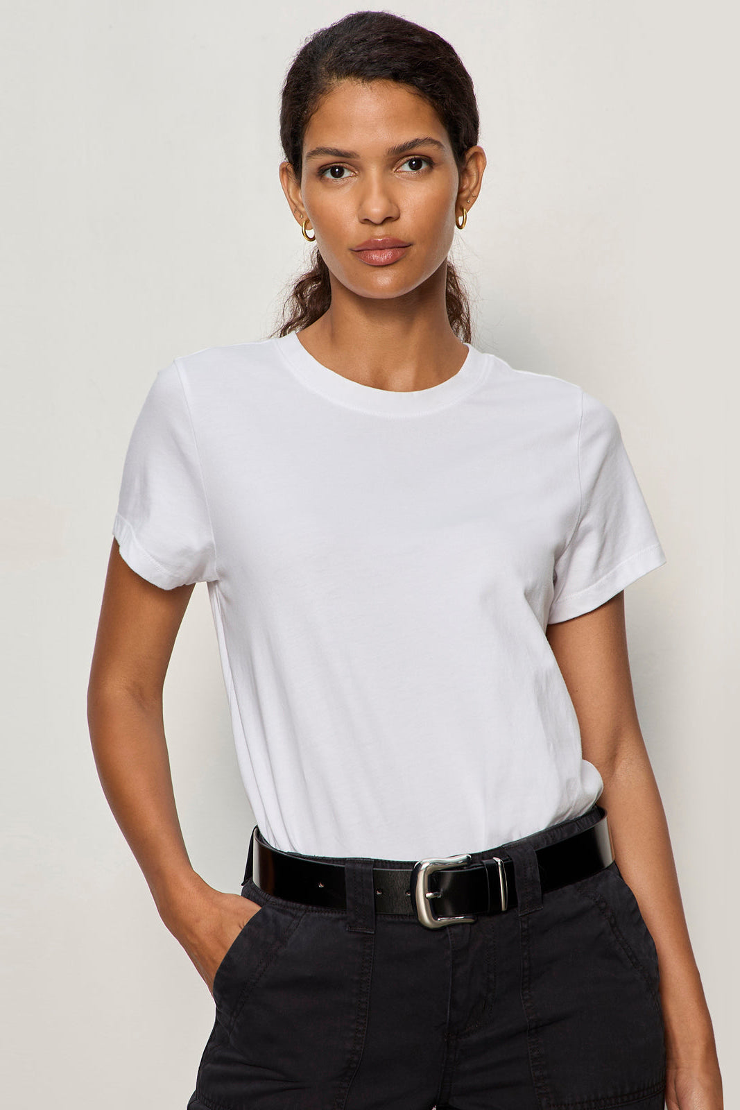 Woman wearing a plain white t-shirt and black pants against a light background