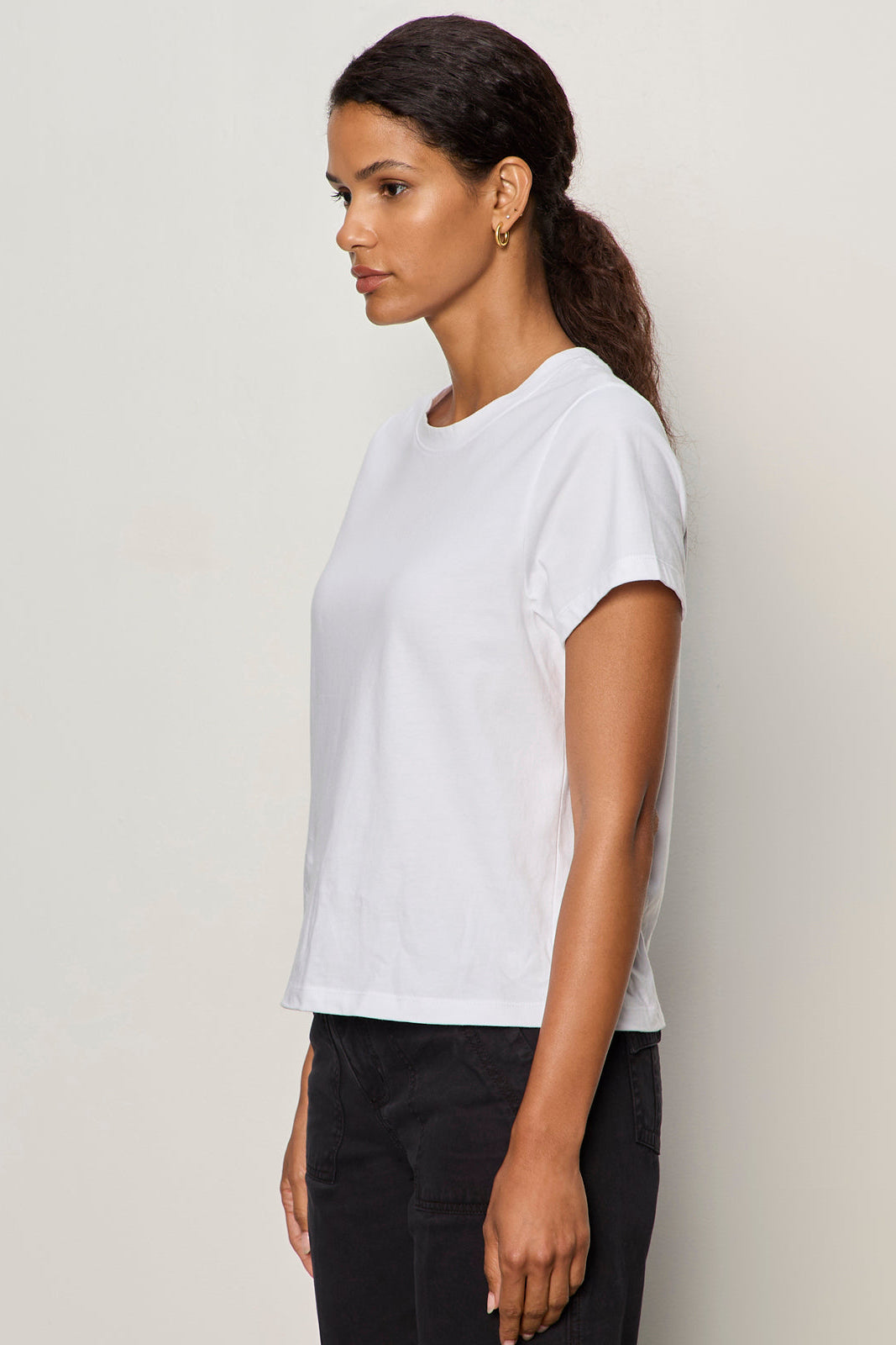 Woman wearing a white t-shirt and black pants against a plain background