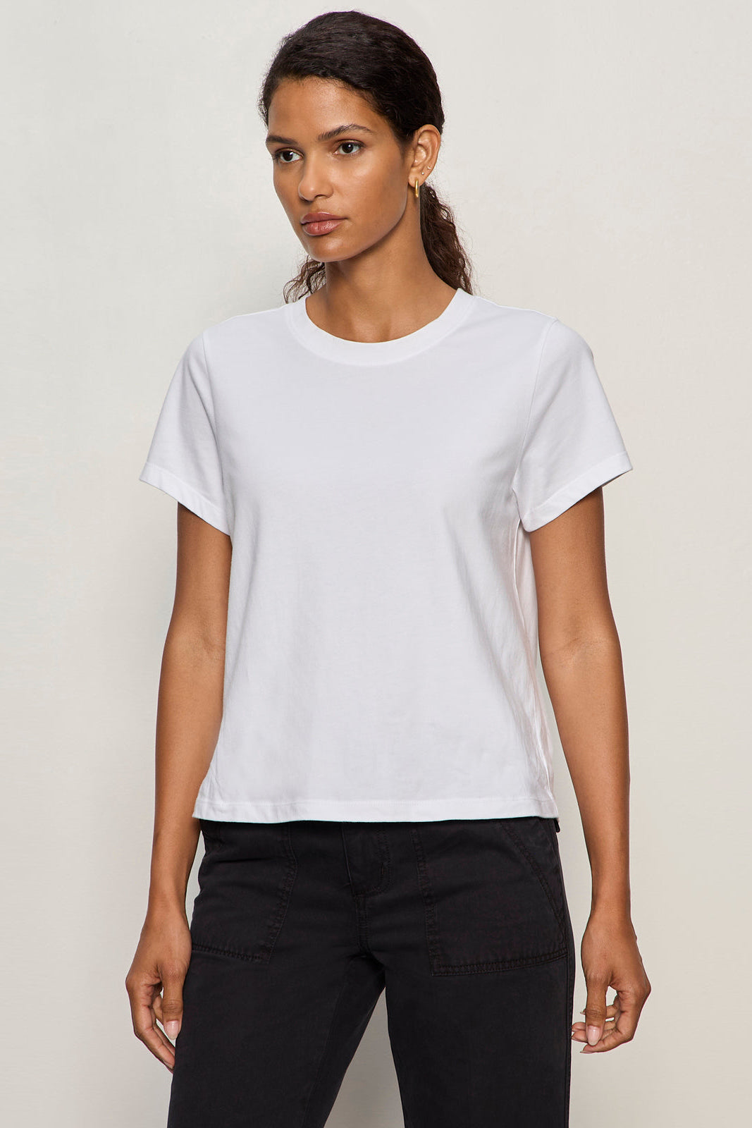Woman wearing a plain white t-shirt and black pants against a light background