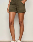 Person wearing olive green shorts with a plain background