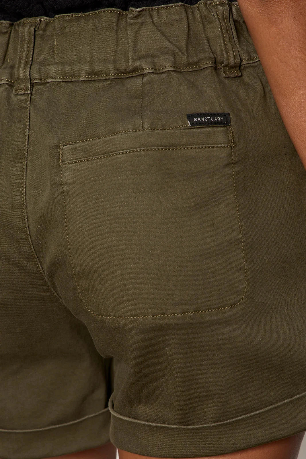 Close-up of olive green shorts with a brand label on the pocket.