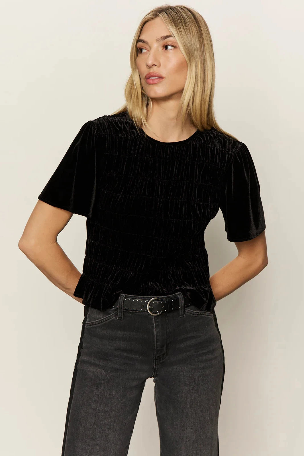 Woman wearing a black textured top and dark jeans against a plain background