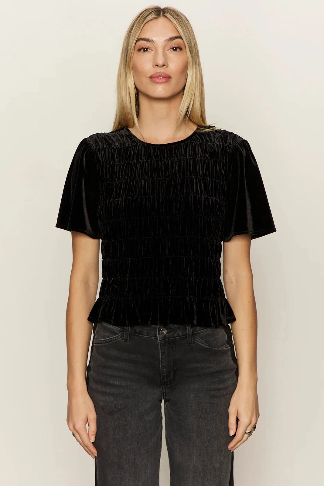 Woman wearing a black pleated top and dark jeans against a plain background