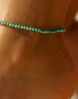 Close-up of a person's ankle with a turquoise beaded anklet against a neutral background