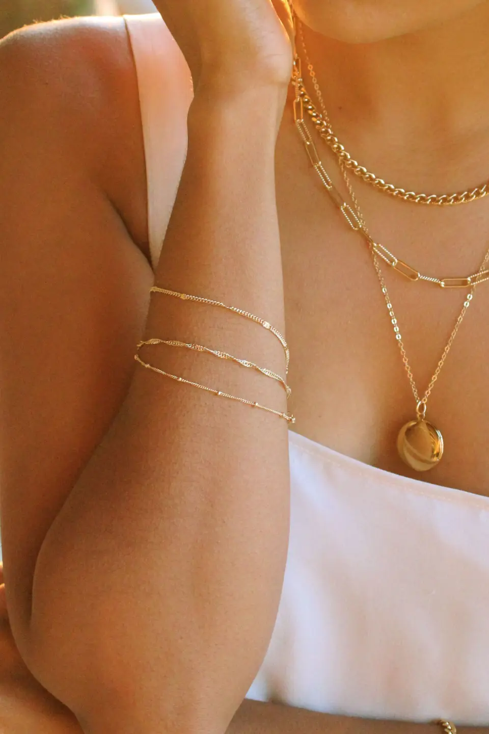 Close-up of a person wearing multiple gold necklaces and an arm band.