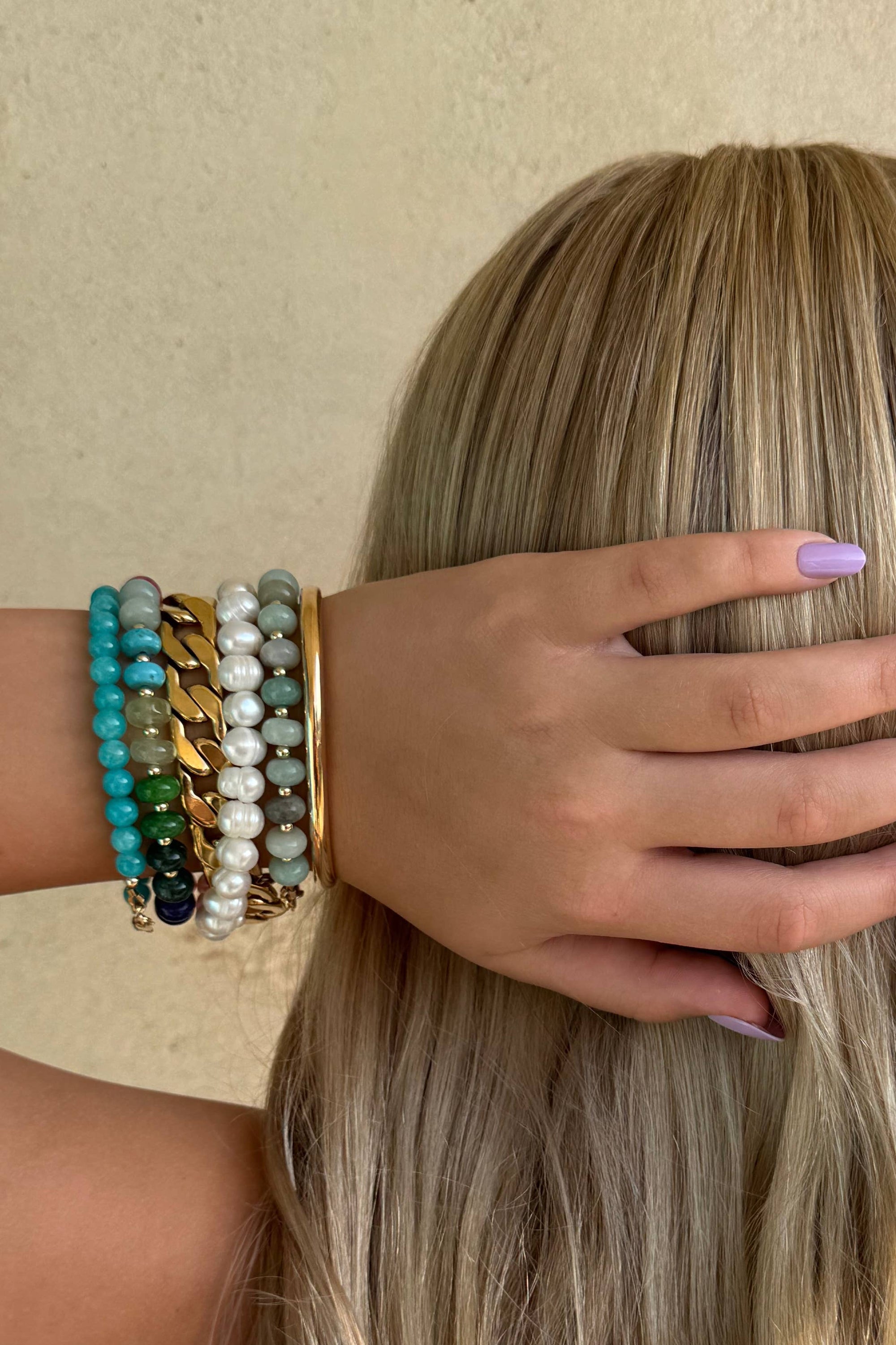 Person with long blonde hair and colorful bracelets on a beige background