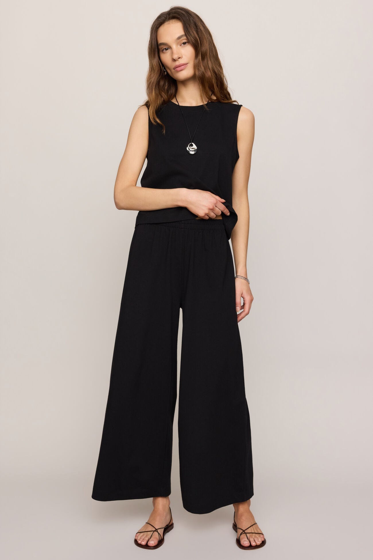 Woman wearing a black sleeveless top and wide-leg pants on a plain background