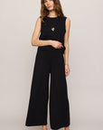 Woman wearing a black sleeveless top and wide-leg pants on a plain background
