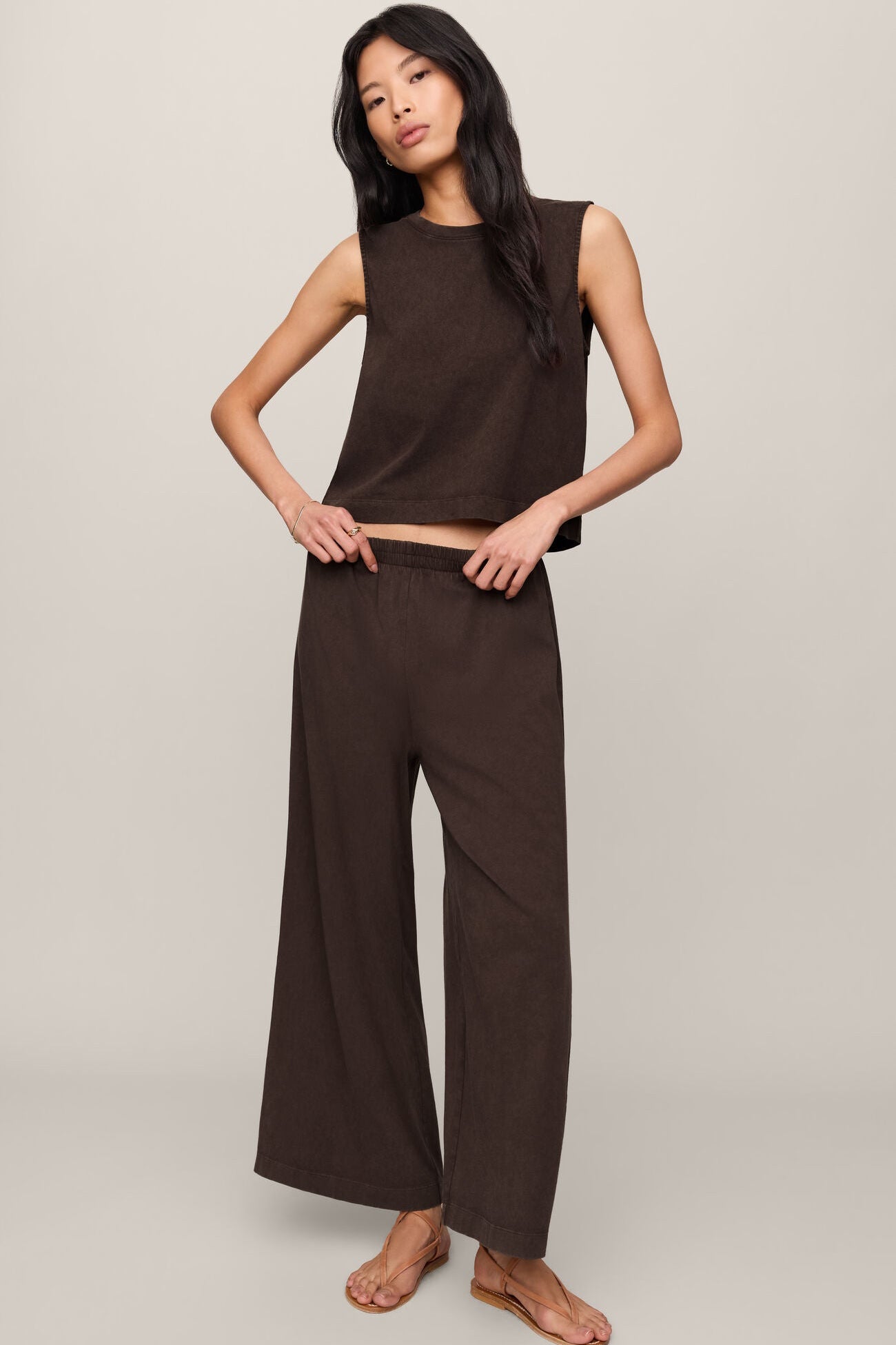 Woman wearing a brown sleeveless top and wide-leg pants on a plain background