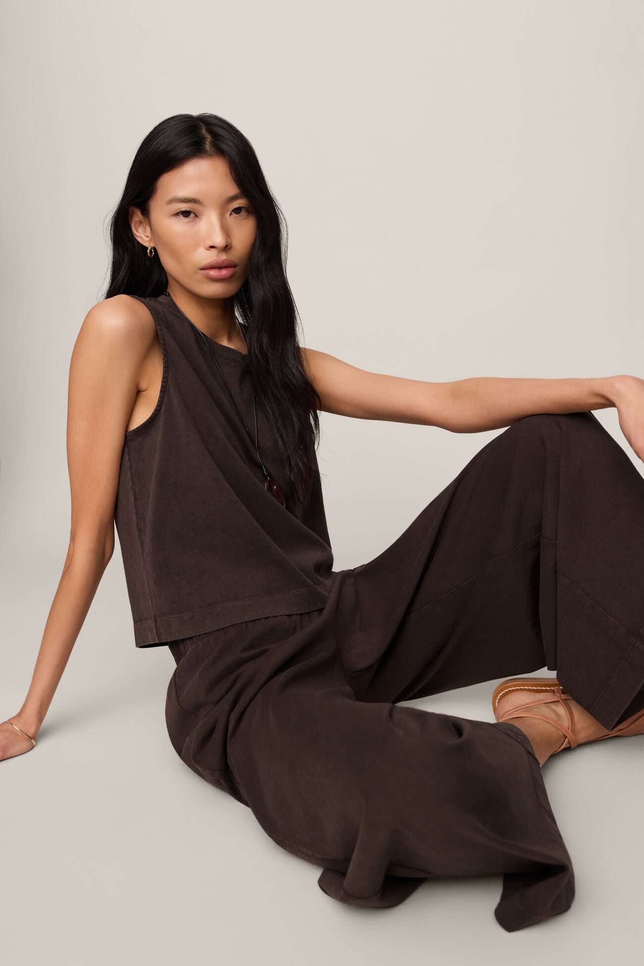 Woman wearing a brown jumpsuit sitting on a light gray background