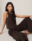 Woman wearing a brown jumpsuit sitting on a light gray background