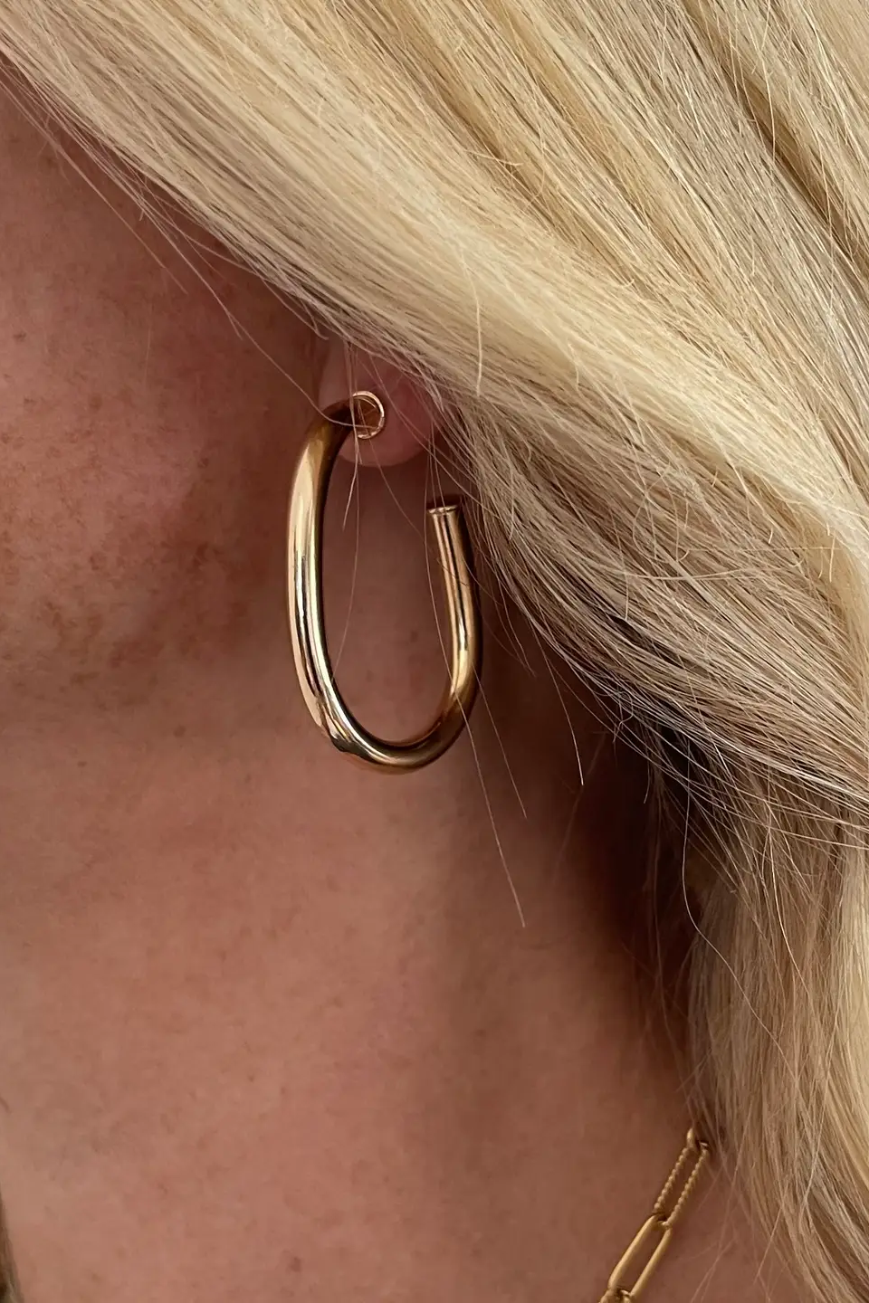 Close-up of a person wearing a gold hoop earring with blonde hair.