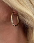 Close-up of a person wearing a gold hoop earring with blonde hair.