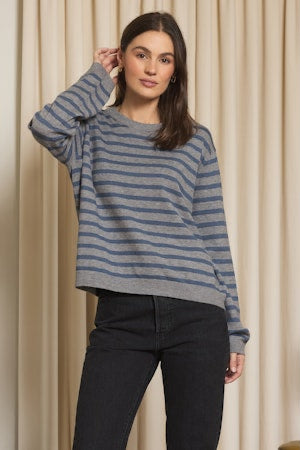 Woman wearing a blue and gray striped sweater against a beige curtain background