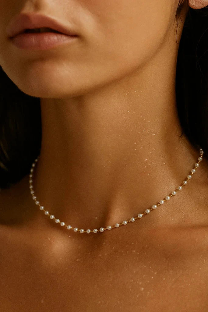 Close-up of a woman wearing a delicate pearl necklace against a neutral background