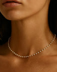 Close-up of a woman wearing a delicate pearl necklace against a neutral background