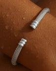 Silver textured bracelet on a wrist with a brown background