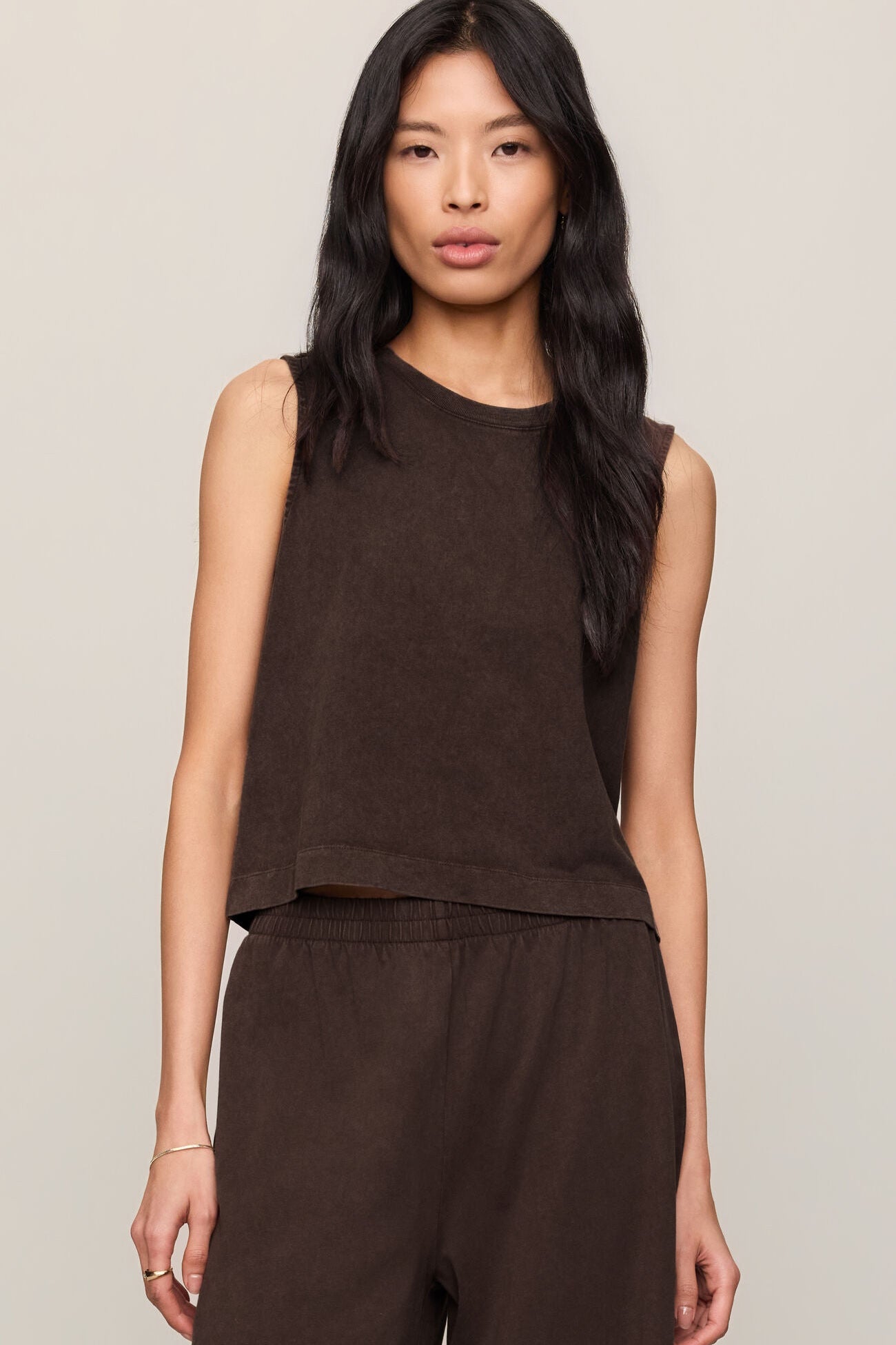 Woman wearing a brown sleeveless top and pants against a neutral background