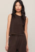 Woman wearing a brown sleeveless top and pants against a neutral background
