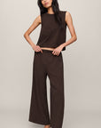 Woman wearing a brown sleeveless top and wide-leg pants on a plain background